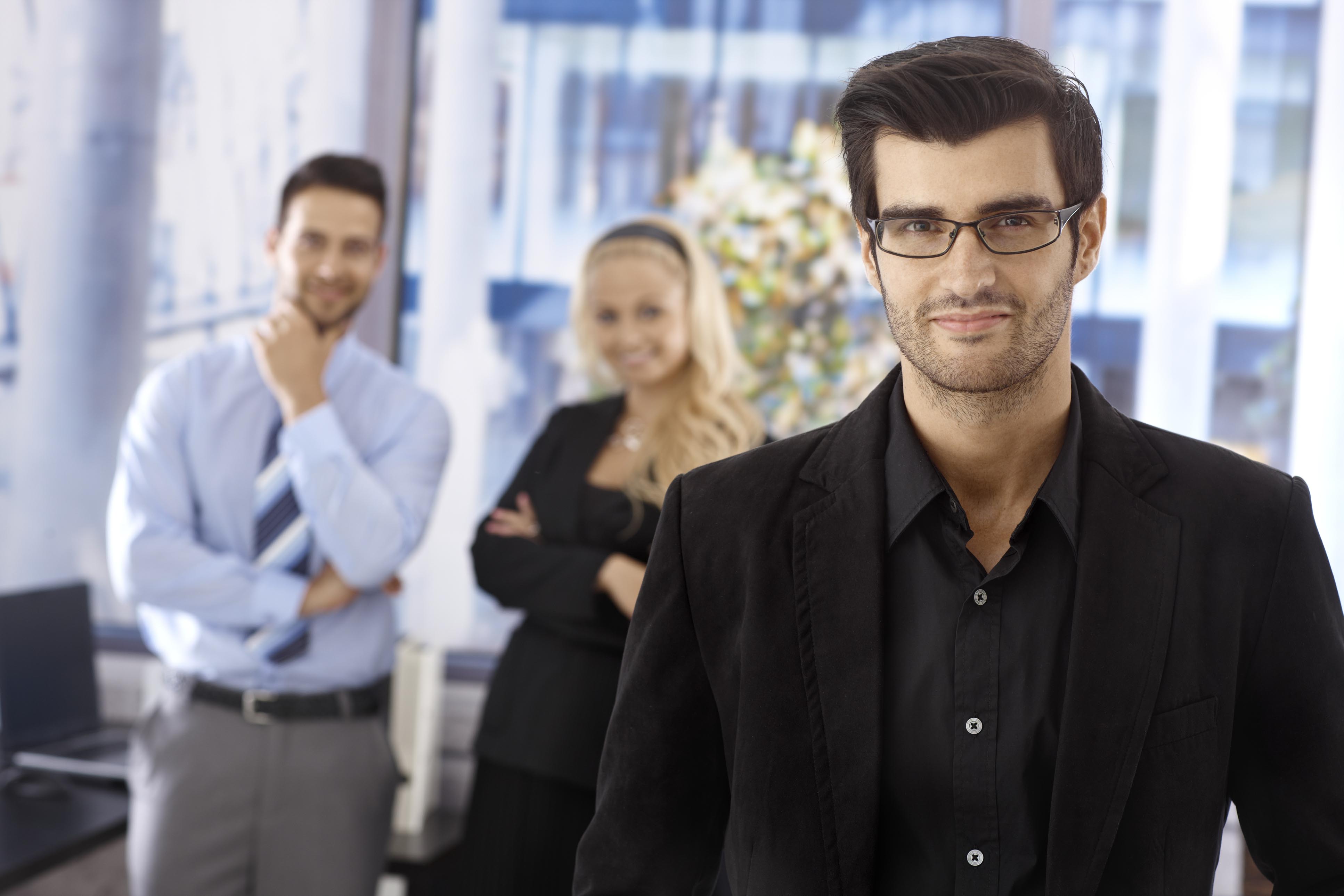 A man with glasses and two collegues in background thinking about how they can develop or train their employees.